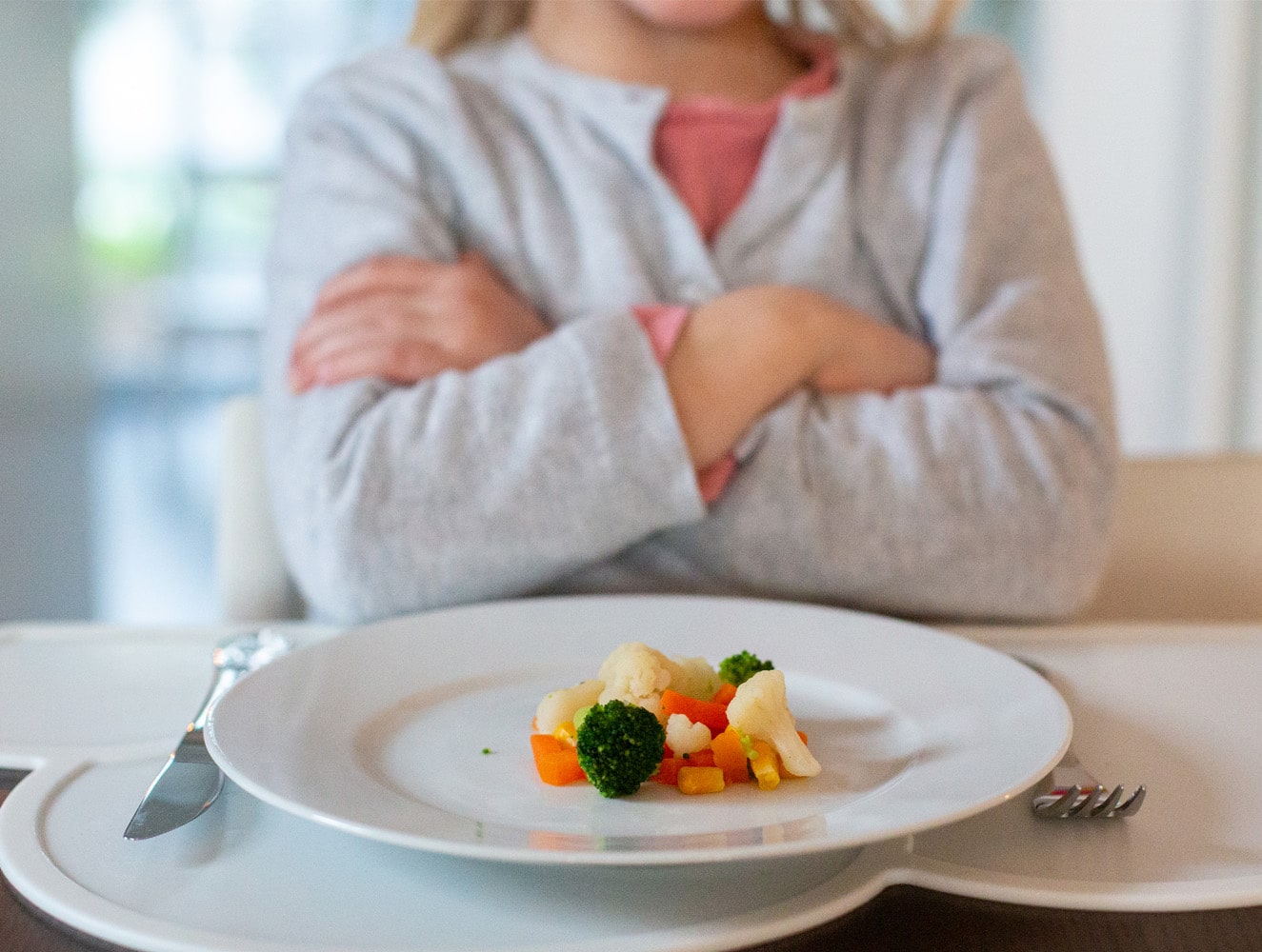 Kind mit verschränkten Armen vor Teller